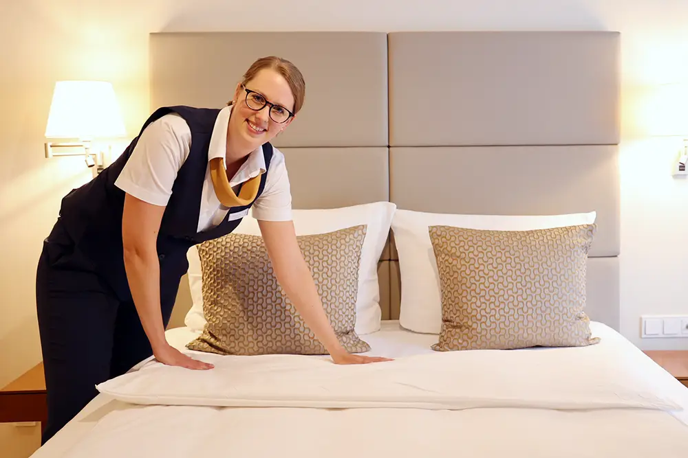 A woman is making up a double bed for upcoming guests